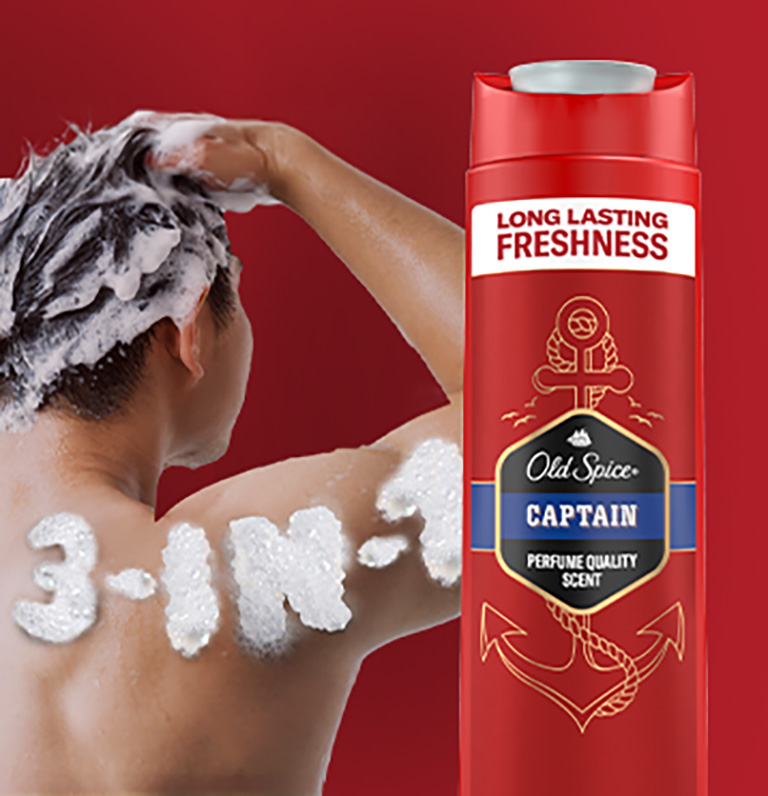 Old Spice Captain 3-in-1 shower gel bottle with red packaging shown next to a man washing his hair, with the words ‘3-IN-1’ written in foam on his back.